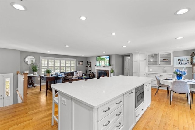 kitchen with stainless steel microwave, a fireplace, white cabinetry, a kitchen island, and light wood-style floors