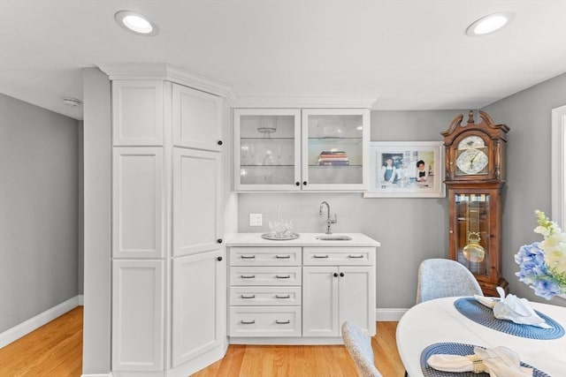 kitchen featuring light wood-type flooring, baseboards, glass insert cabinets, light countertops, and white cabinetry