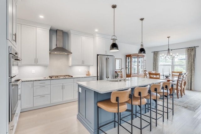 51 Tinkers Blf Unit 51, Plymouth, MA 02360 - kitchen featuring wall chimney range hood, a sink, stainless steel appliances, light wood finished floors, and decorative backsplash