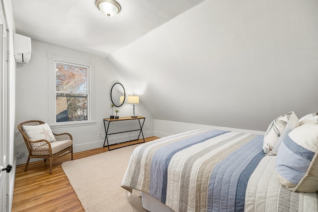 bedroom featuring light wood-type flooring, an AC wall unit, and vaulted ceiling