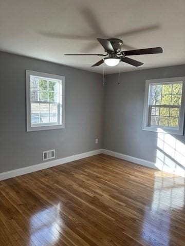 empty room featuring a ceiling fan, visible vents, wood finished floors, and baseboards