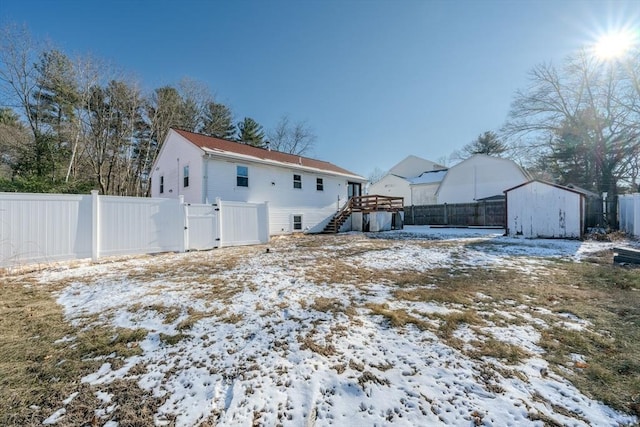 snow covered back of property with a storage unit and a deck