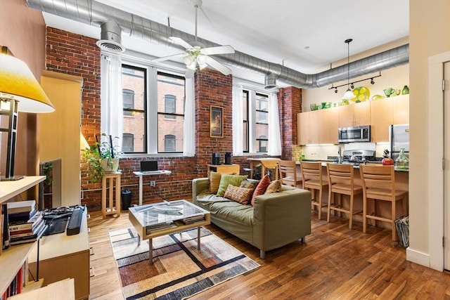 living area featuring a ceiling fan, brick wall, wood finished floors, and a towering ceiling