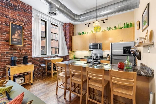 kitchen featuring a peninsula, appliances with stainless steel finishes, a kitchen bar, and light wood-style floors