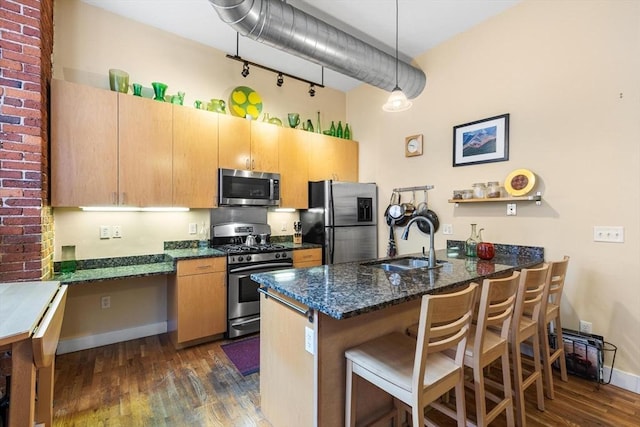 kitchen featuring dark wood-style flooring, a sink, a peninsula, dark stone counters, and stainless steel appliances