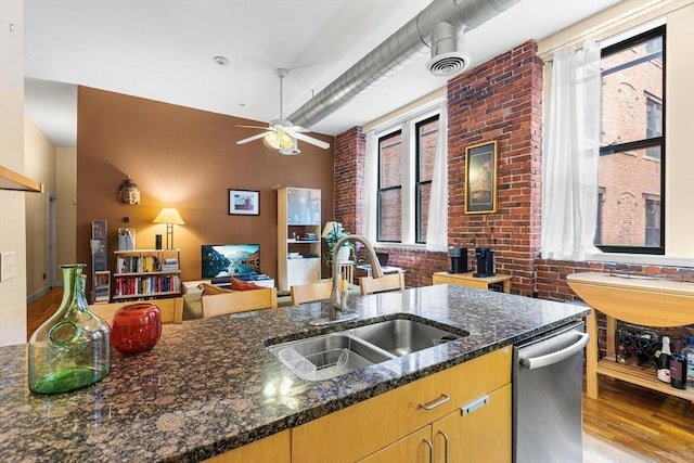 kitchen featuring stainless steel dishwasher, a ceiling fan, light wood-style floors, dark stone counters, and a sink