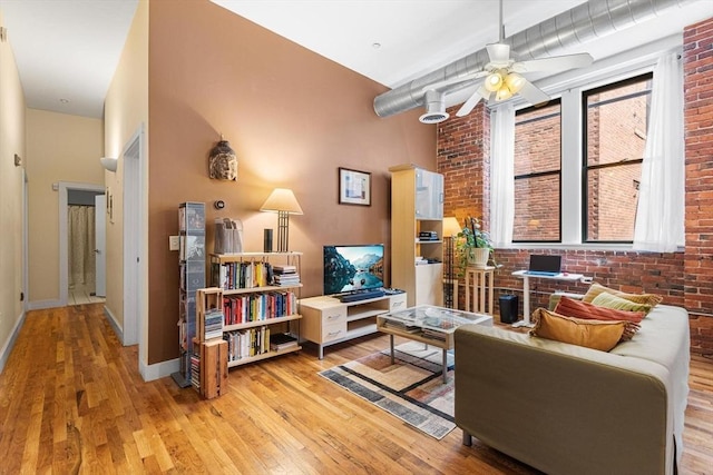 sitting room with ceiling fan, brick wall, baseboards, and light wood-style floors