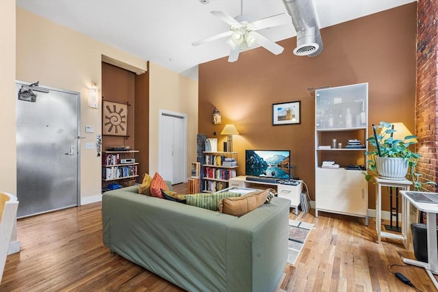 living area featuring baseboards, a high ceiling, a ceiling fan, and wood finished floors