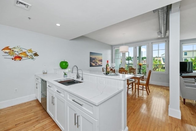 kitchen with white cabinetry, sink, stainless steel dishwasher, light stone counters, and kitchen peninsula