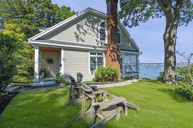 back of house with a chimney, a yard, and a water view
