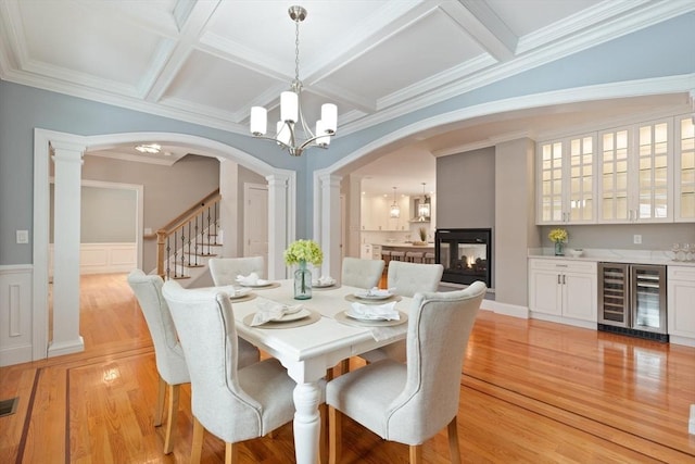 dining area with arched walkways, beverage cooler, light wood finished floors, and ornate columns