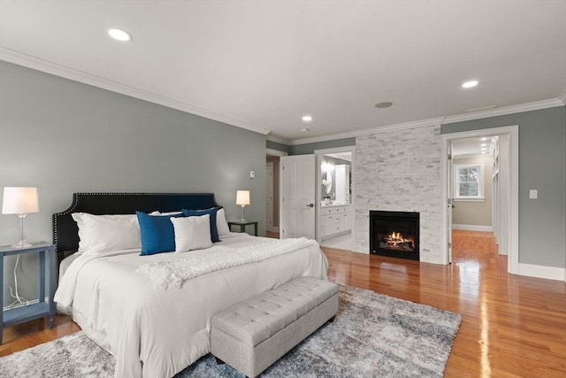 bedroom featuring crown molding, baseboards, wood finished floors, and a stone fireplace