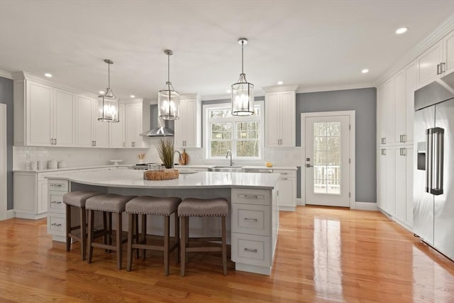 kitchen with built in refrigerator, wall chimney exhaust hood, white cabinets, and light countertops