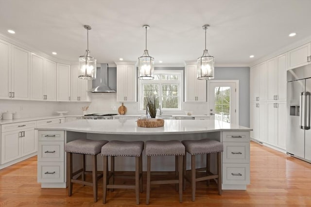 kitchen featuring wall chimney exhaust hood, stainless steel built in refrigerator, light countertops, and white cabinetry