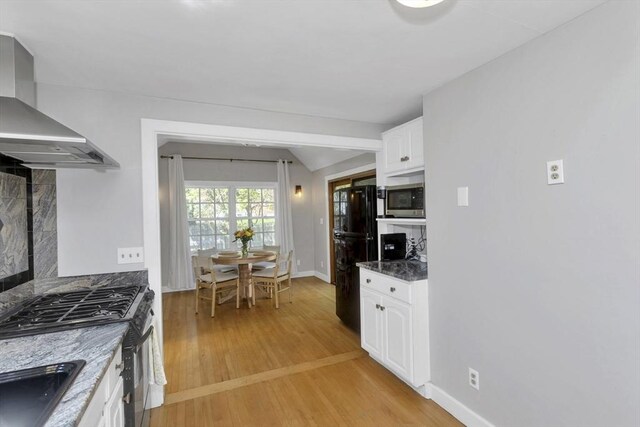 kitchen with baseboards, wall chimney exhaust hood, white cabinets, light wood-style flooring, and stainless steel appliances