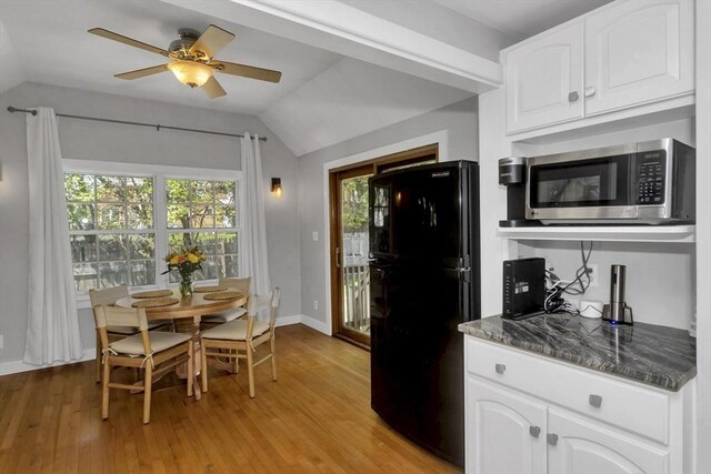kitchen with freestanding refrigerator, stainless steel microwave, white cabinetry, and lofted ceiling