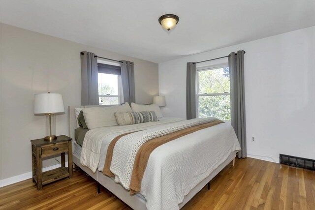 bedroom with baseboards, visible vents, and wood finished floors