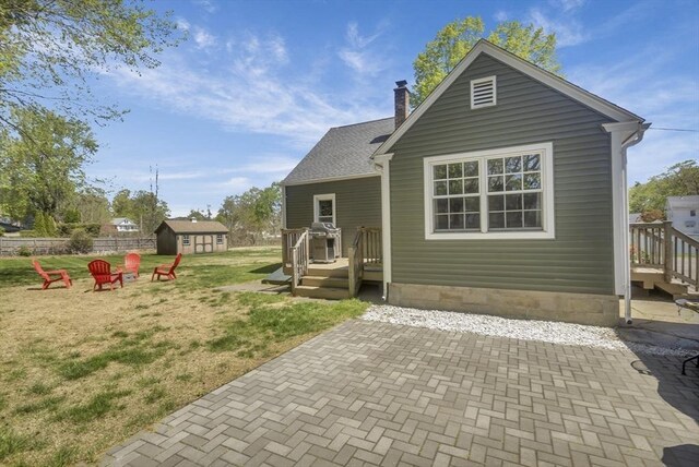 back of property with a chimney, a lawn, an outbuilding, fence, and a patio