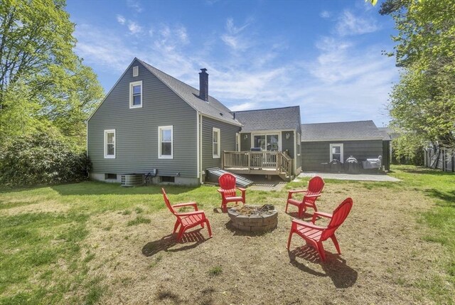 rear view of property with a fire pit, a wooden deck, roof with shingles, a chimney, and a yard