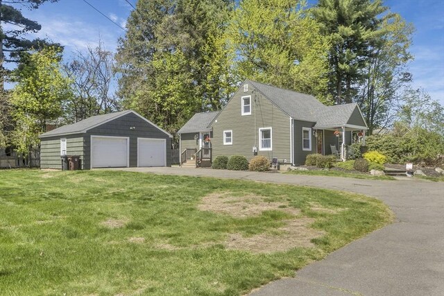 view of front of property with a detached garage, roof with shingles, an outdoor structure, and a front yard