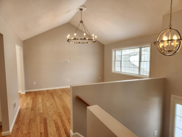 hallway with light wood-style floors, lofted ceiling, an upstairs landing, and an inviting chandelier