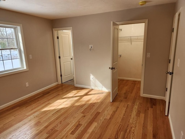 unfurnished bedroom featuring light wood finished floors, a closet, a walk in closet, and baseboards