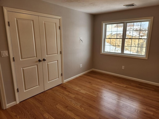 unfurnished bedroom featuring a closet, visible vents, baseboards, and wood finished floors