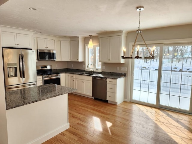 kitchen with stainless steel appliances, decorative light fixtures, a sink, and light wood-style flooring