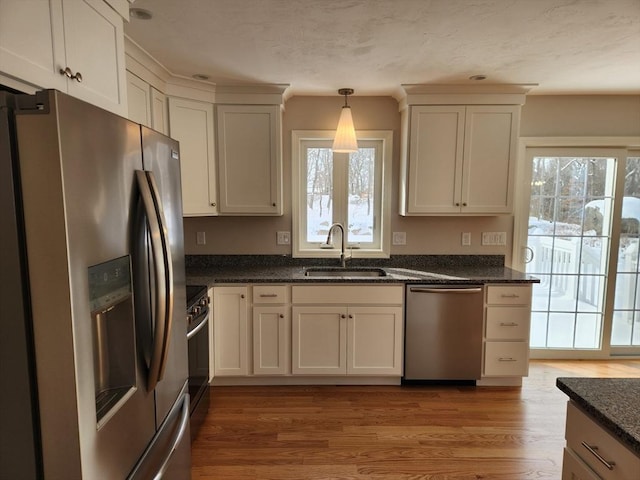 kitchen featuring decorative light fixtures, stainless steel appliances, dark stone counters, a sink, and light wood-type flooring