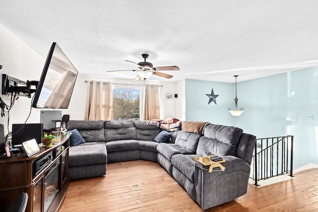 living room featuring ceiling fan, light hardwood / wood-style flooring, and a textured ceiling