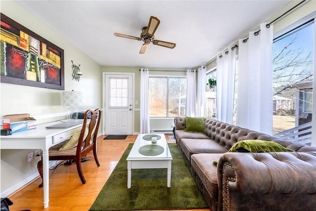 living room featuring baseboard heating, baseboards, light wood-type flooring, and a ceiling fan