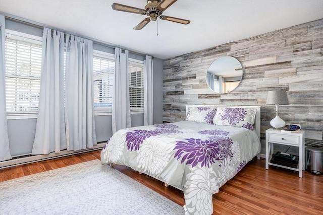 bedroom with a baseboard radiator, a ceiling fan, wood finished floors, and an accent wall