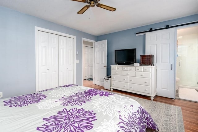 bedroom featuring connected bathroom, ceiling fan, a barn door, wood finished floors, and a closet