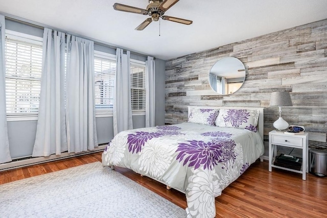 bedroom with an accent wall, a baseboard heating unit, a ceiling fan, and wood finished floors