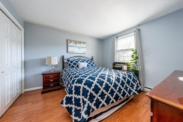 bedroom with wood finished floors, a closet, baseboard heating, and baseboards