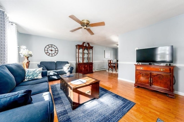 living room with baseboard heating, baseboards, light wood-style floors, and a ceiling fan