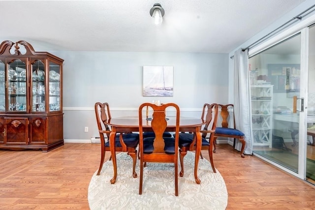 dining space featuring light wood-style flooring, a textured ceiling, and baseboards