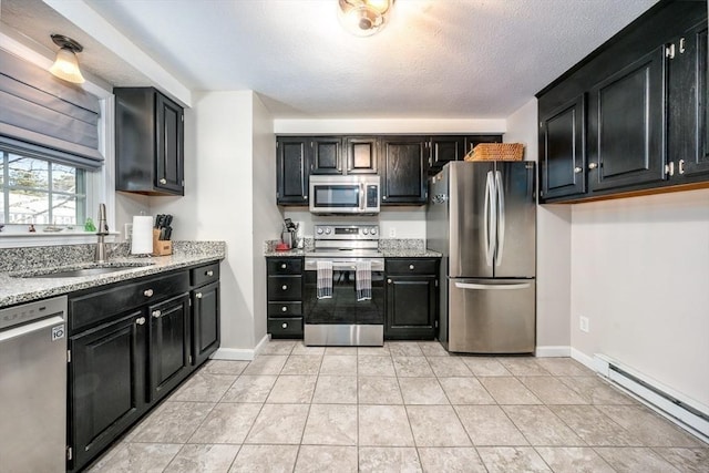 kitchen with a sink, baseboard heating, appliances with stainless steel finishes, and dark cabinets