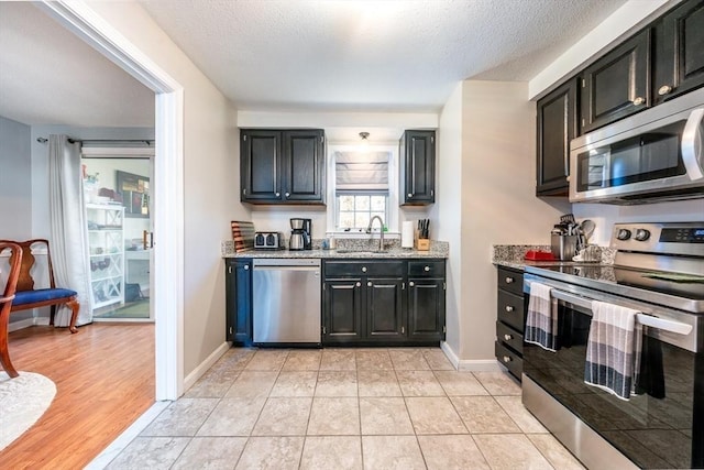 kitchen featuring dark cabinetry, light stone countertops, appliances with stainless steel finishes, and a textured ceiling