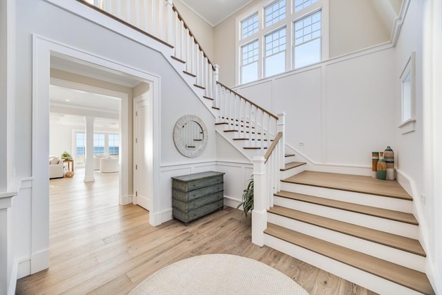 stairway with hardwood / wood-style floors, a towering ceiling, ornamental molding, and decorative columns