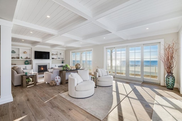 living room with coffered ceiling, a water view, built in features, beam ceiling, and light hardwood / wood-style flooring