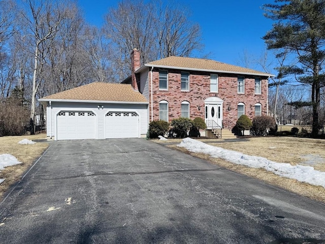 colonial inspired home featuring brick siding, driveway, a chimney, and an attached garage