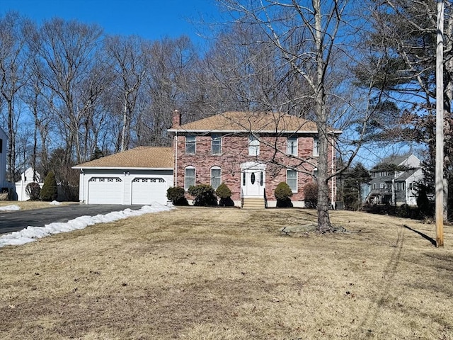 colonial-style house with entry steps, aphalt driveway, an attached garage, brick siding, and a front yard