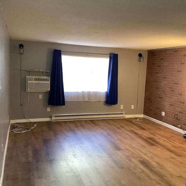 empty room with a baseboard heating unit, a wall unit AC, wood-type flooring, a textured ceiling, and brick wall