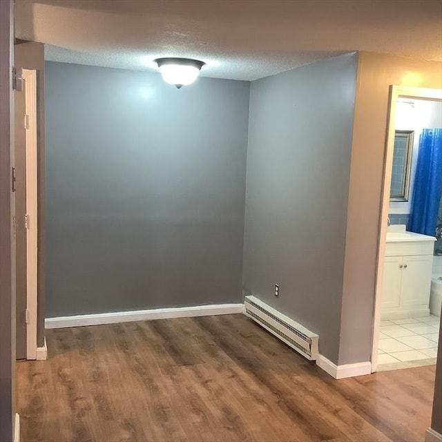 unfurnished room featuring light hardwood / wood-style flooring, a baseboard radiator, and a textured ceiling