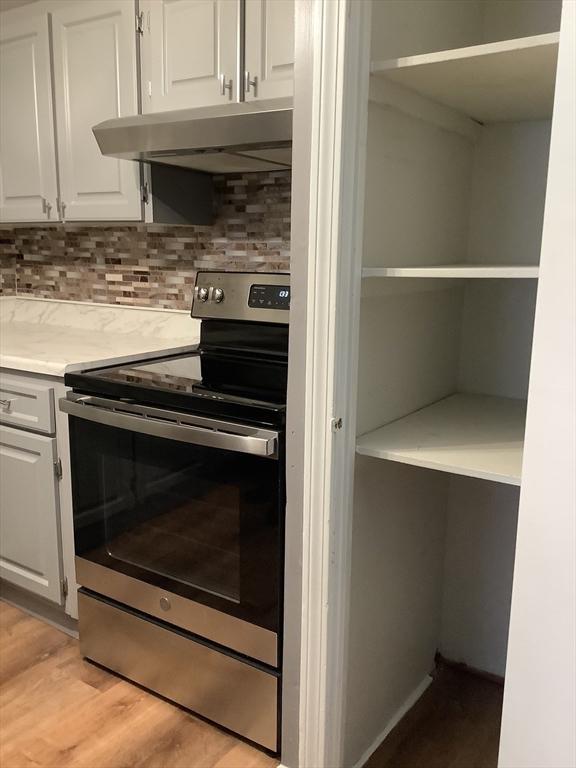 kitchen with electric stove, backsplash, light wood-type flooring, and white cabinets