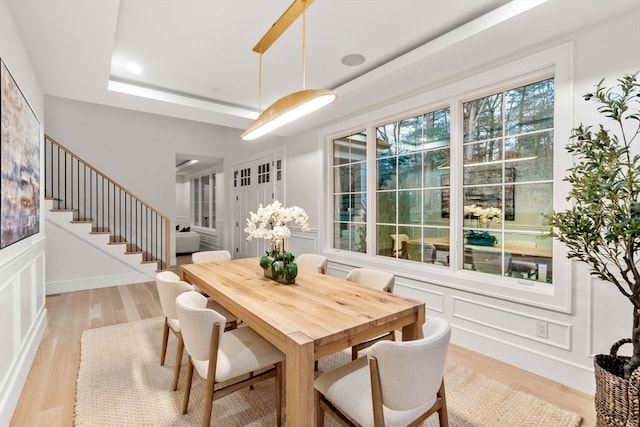 dining room featuring light wood-type flooring, stairs, a tray ceiling, and a decorative wall