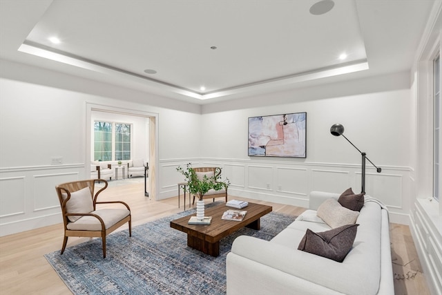 living area with light wood finished floors, a tray ceiling, and a decorative wall