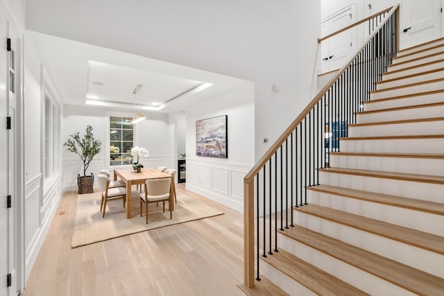 dining area with light wood-style flooring, stairway, a raised ceiling, and a decorative wall