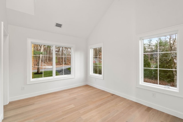 spare room with lofted ceiling, light wood-type flooring, visible vents, and baseboards